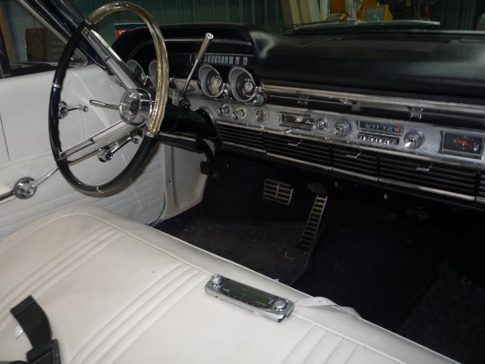 White bench seat and chrome dash inside a 1960s Mercury with loose stereo on the seat
