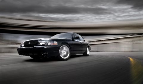 2003 Mercury Marauder - A black 2003 Mercury Marauder is captured in motion on a winding road under a dramatic sky.