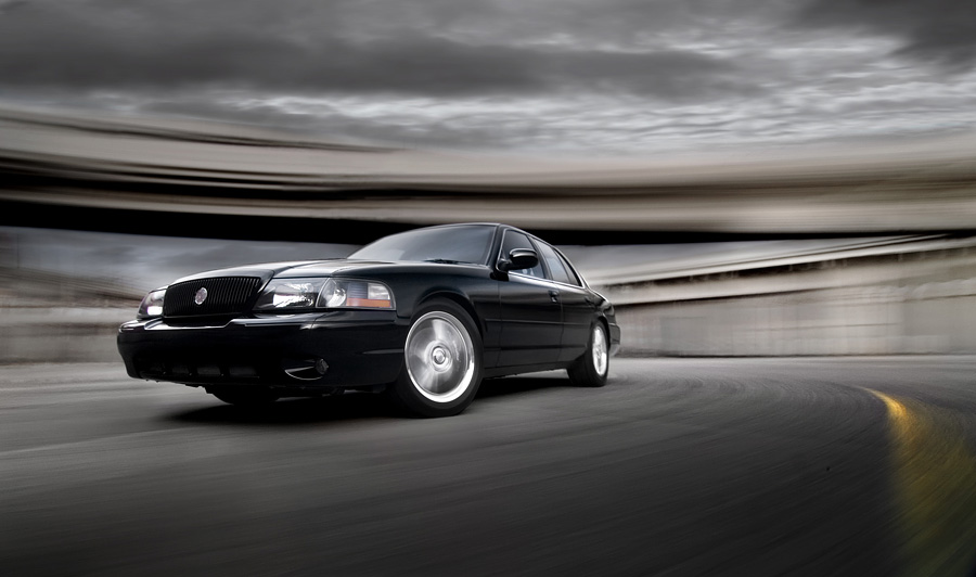 Black full-size sedan in motion on a curved road, front 3/4 view with motion-blurred background
