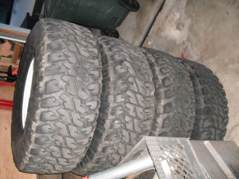 1991 Ford Bronco - A set of four off-road tires are lined up, showing their deep, aggressive tread patterns.