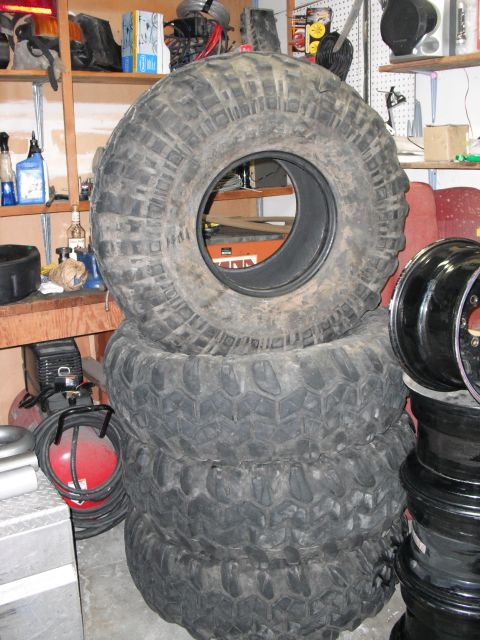 1991 Ford Bronco - A pile of four large off-road tires are stacked in a garage setting.