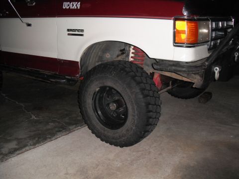 1991 Ford Bronco - The front fender and tire of a two-tone red and white Ford Bronco are visible.