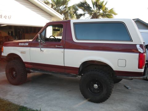 1991 Ford Bronco - Side view of a lifted 1991 Ford Bronco with two-tone paint and off-road tires.