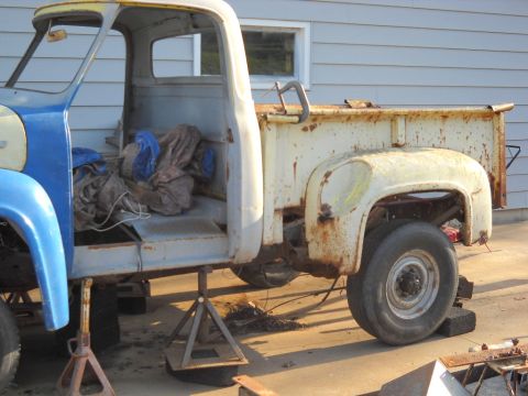 1954 Ford F-100 - Ford F-100 truck body undergoing restoration, supported by jack stands. Visible parts include the cab, bed, and front fender.