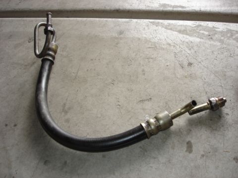 1992 Ford Bronco - A power steering hose with metal fittings is shown against a concrete background. The part is not a vehicle.