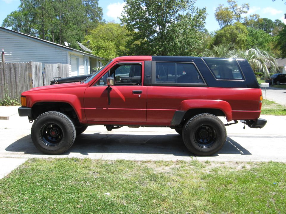 Red Toyota 4Runner with black rear top, side view, lifted on black steel wheels in a driveway