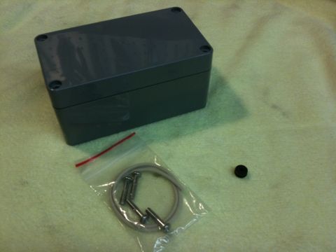 Suzuki Samurai - A gray electrical enclosure is shown with its hardware, including screws and a rubber plug, laid out on a textured surface.