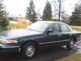 1997 Ford Crown Victoria sedan, dark green, parked outside on a cloudy day