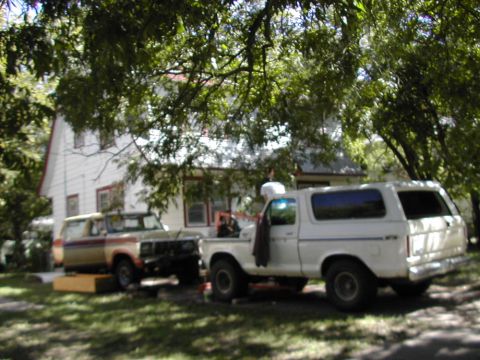 1979 Ford Bronco - Two Ford Broncos are parked in a grassy yard in front of a house, with one undergoing some work.