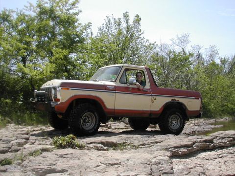 1979 Ford Bronco - Driver poses in a two-tone Ford Bronco on a rocky terrain next to a body of water.