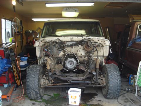 1979 Ford Bronco - A white 1979 Ford Bronco sits in a garage with its front end disassembled, revealing the engine and transmission components.