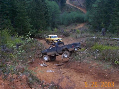 1983 Ford Bronco - Two trucks navigate a steep, muddy trail through a wooded area.