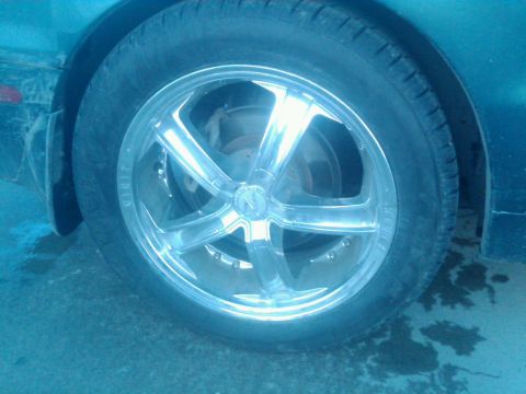 1987 Suzuki Samurai - Close-up of a chrome wheel and tire on a teal vehicle, with visible water stains on the ground.