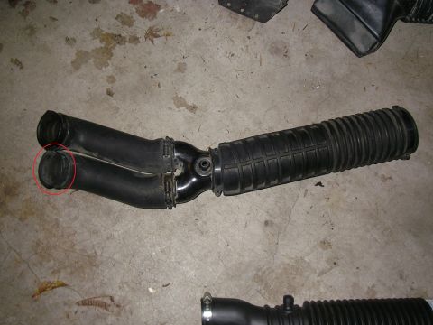 1990 Ford Bronco - Automotive air intake tube with accordion bellows and split outlet, circled defect, on a concrete shop floor.