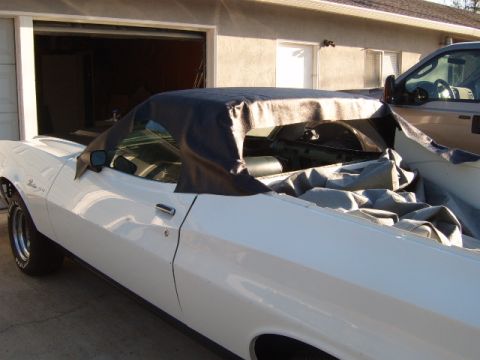 1973 Ford Ranchero - A white coupe is partially covered in front of a garage, with a pickup truck visible to the right.