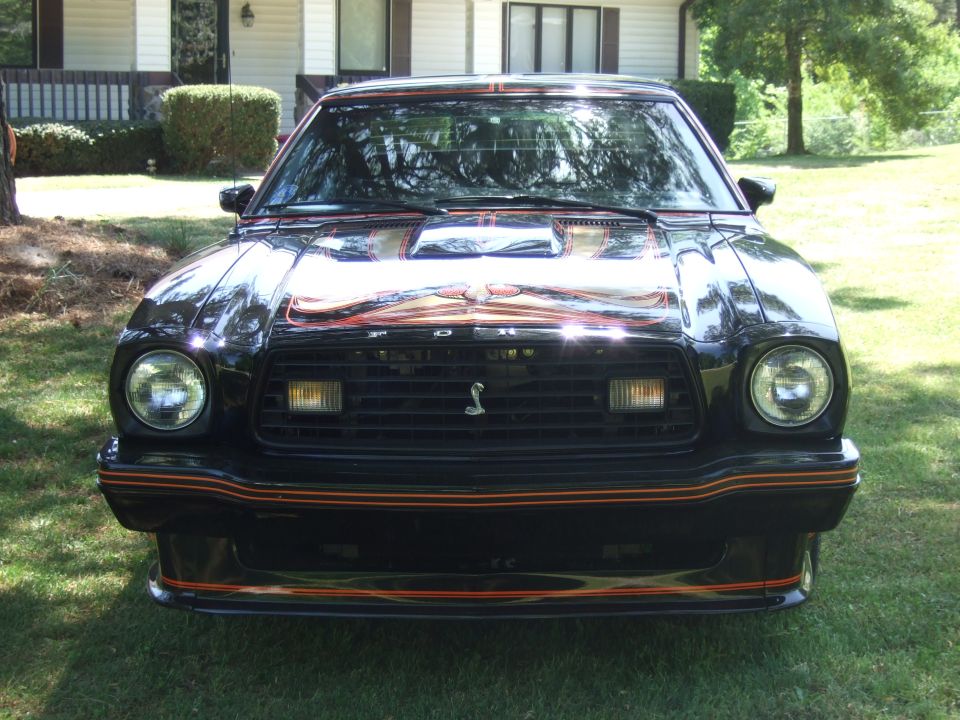 Front view of a black 1978 Ford Mustang II with orange racing stripes and a Cobra emblem