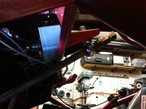 Suzuki Samurai - Tight low-angle shot under a red tube-frame buggy in a home shop, showing a chrome heim-joint link mounted to a bracket on the red tubing a…