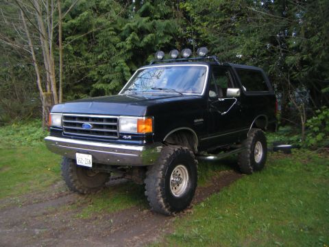 Black lifted 1990 Ford Bronco with roof lights and off-road tires parked on grass
