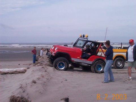 1983 Ford Bronco - Two vehicles, a red Jeep Wrangler and a yellow pickup truck, are parked on a sandy beach near the ocean.
