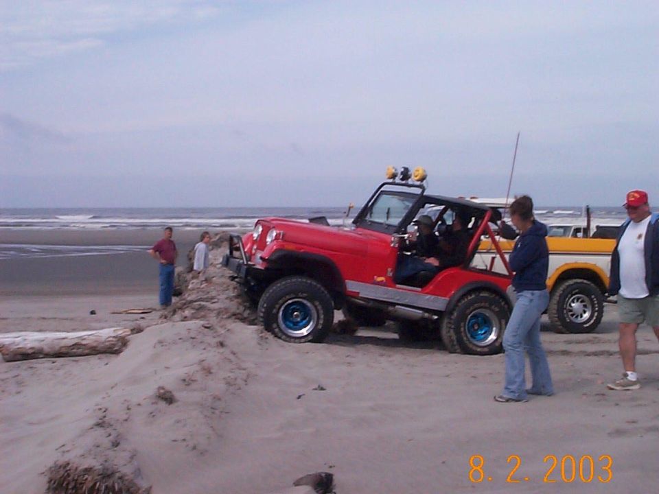 Red topless Jeep CJ on a beach with people, yellow-and-white Bronco at right