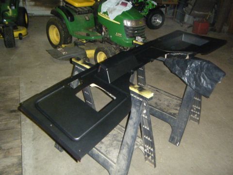 Black dashboard section on sawhorses with two green lawn tractors in background