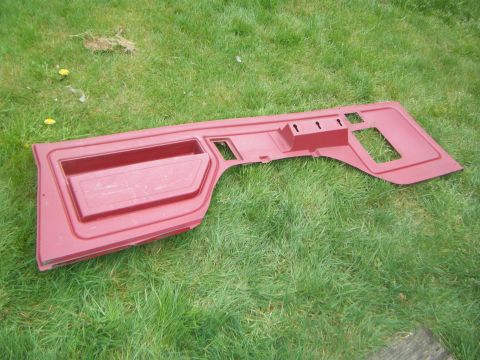 Red car door panel with storage pocket and cutouts, lying on grass