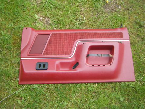 Red car door panel with fabric insert and chrome trim, lying on grass