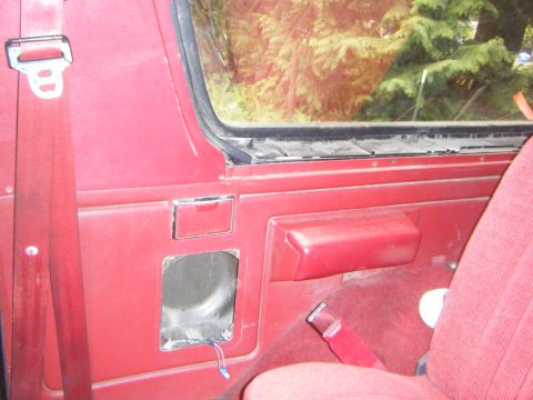 1990 Ford Bronco — Red interior door panel with a removed speaker grille and red seatbelt