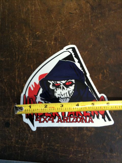 Suzuki Samurai - Die-cut "Undertakers 4x4 Arizona" club decal featuring red-eyed hooded skull artwork in blue, red and black, laid on a scratched dark workb…