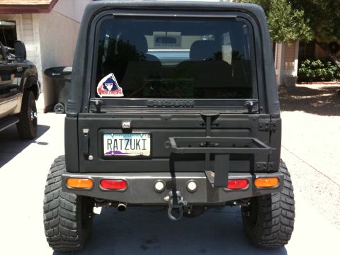 Suzuki Samurai - Rear view of a flat-black Suzuki Samurai hardtop on a driveway, wearing an Arizona vanity plate reading RATZUKI and a custom rear bumper wi…