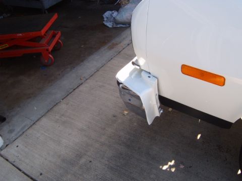 1973 Ford Ranchero - A white vehicle's front bumper is damaged, with white plastic trim hanging loose.