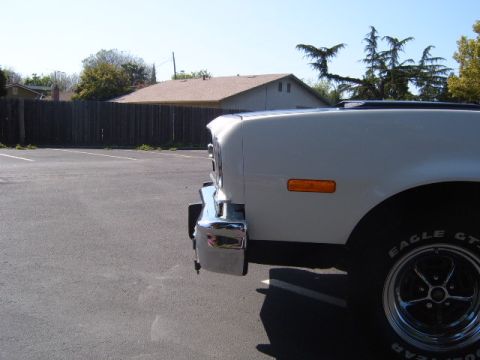 1973 Ford Ranchero - The front corner of a white vehicle is shown from a low angle, revealing a chrome bumper and an orange turn signal.