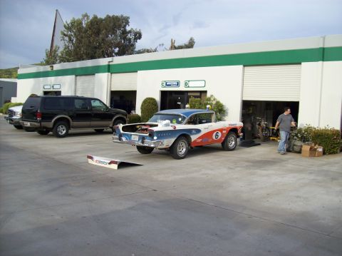 1990 Ford Bronco - A vintage Ford sedan, modified for racing, sits in front of a commercial building with a black SUV nearby.