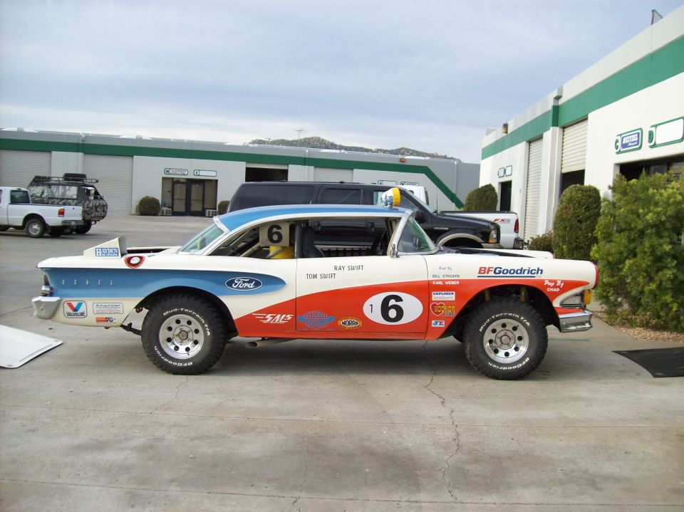 Side view of orange-white-blue number 6 vintage Ford race car on off-road tires
