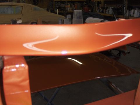 1980 Chevrolet Camaro - A freshly painted orange car spoiler with white racing stripes is shown in a workshop.