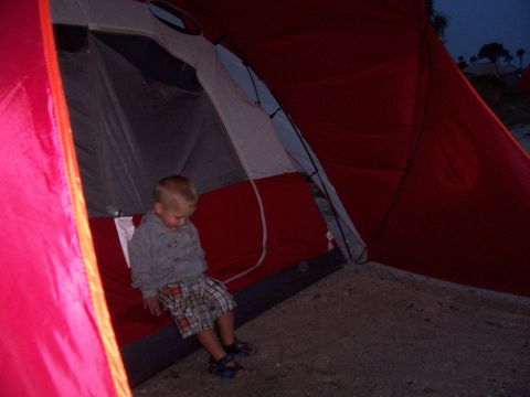 1994 Ford Bronco - A young child sits on the red sleeping pad inside a large tent, with the entrance open to a dusky outdoor scene.