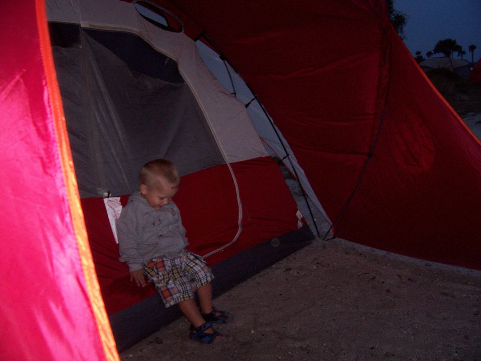 Child sitting inside a red and gray tent