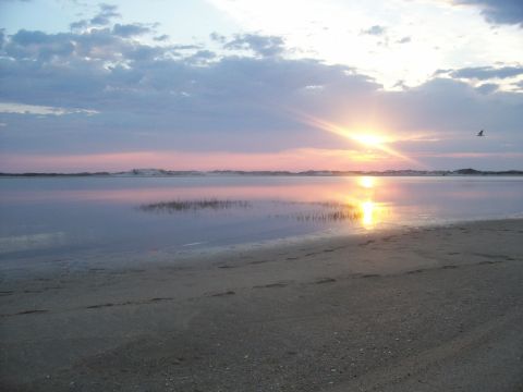 1994 Ford Bronco - A tranquil beach scene unfolds as the sun dips below the horizon, casting a warm glow across the water and sky.