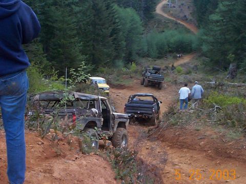 1983 Ford Bronco - Several off-road vehicles navigate a steep dirt track through a forest.