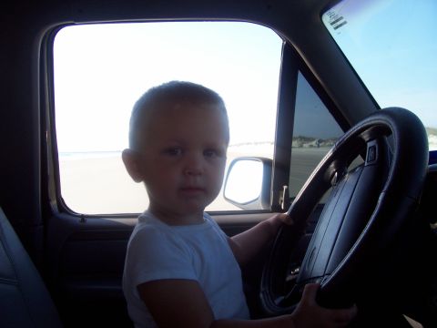 1994 Ford Bronco - A young child sits behind the steering wheel of a vehicle with a beach visible outside the window.