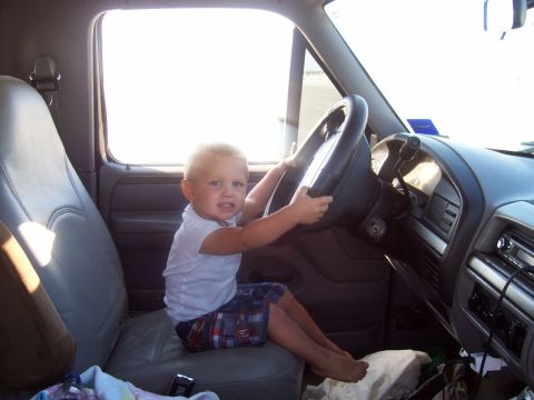 1994 Ford Bronco - A young child sits in the driver's seat of a vehicle, gripping the steering wheel.