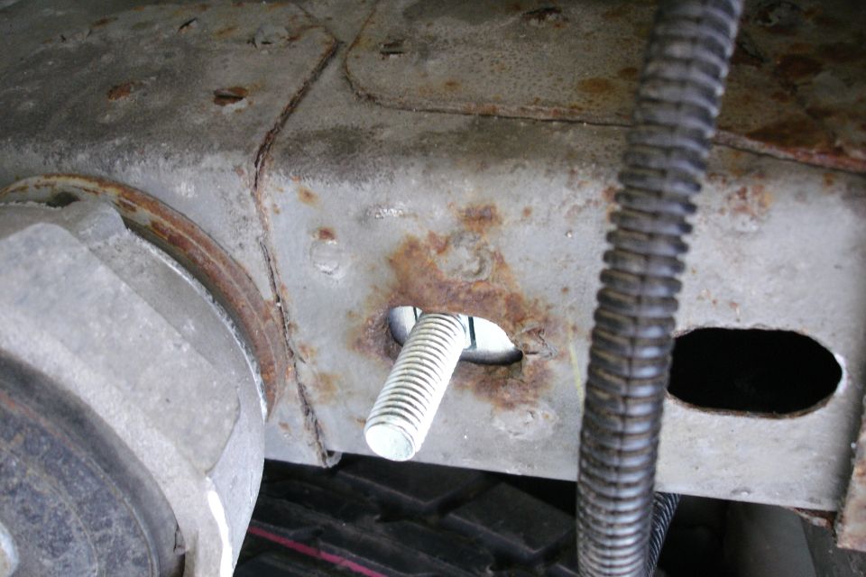 Rusty underbody bracket with a plated bolt through a corroded mounting boss
