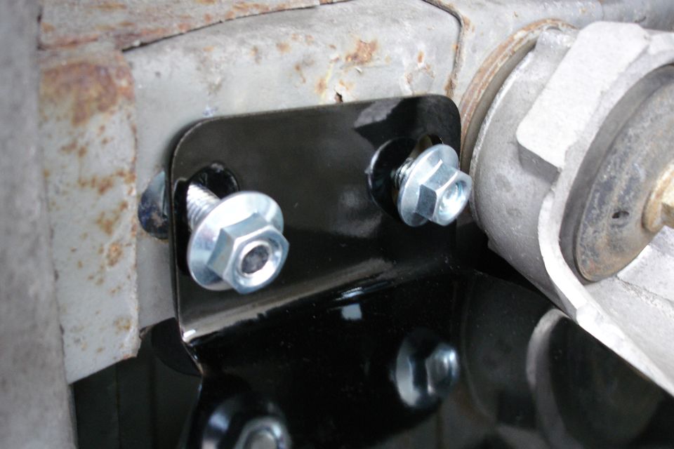 Black steel mounting bracket held by zinc flange bolts against rusty cast surface