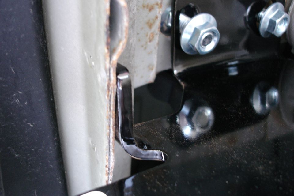 Black steel bracket bolted with zinc hardware next to a rust-edged panel