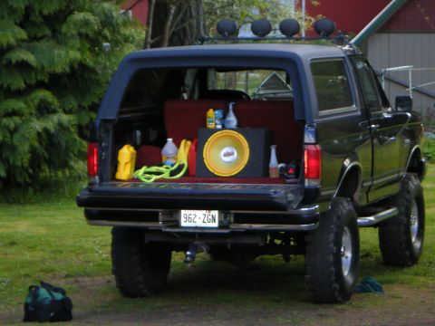 1990 Ford Bronco — Black SUV with lifted suspension, rear open with subwoofer and supplies. License plate 962-ZGN