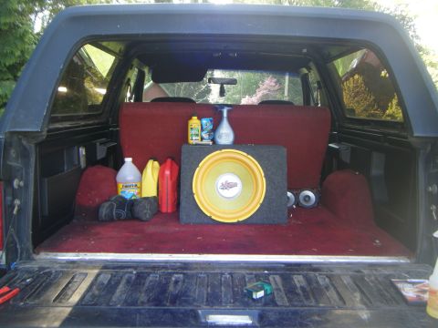 Interior cargo area of a Ford Bronco showing a subwoofer, cleaning supplies, and red seats