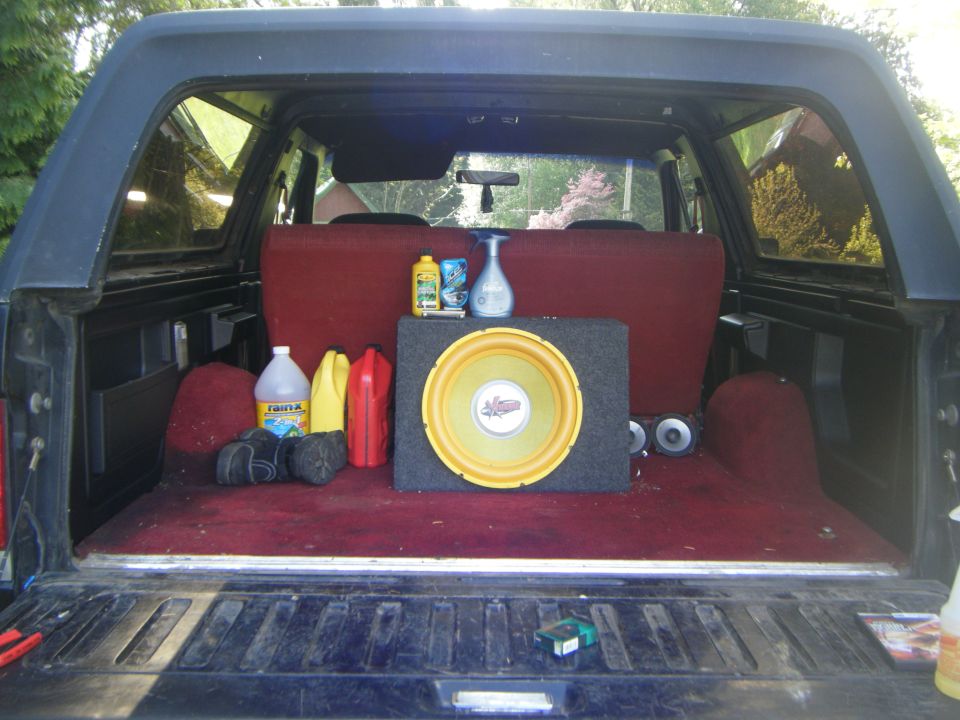 Interior cargo area of a Ford Bronco showing a subwoofer, cleaning supplies, and red seats