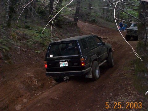 1983 Ford Bronco - A black Toyota 4Runner navigates a muddy off-road trail with another vehicle visible in the background.