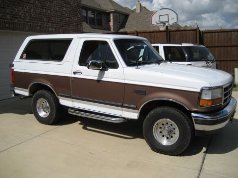 1993 Ford Bronco parked in driveway, white with brown trim. Another SUV is parked behind it