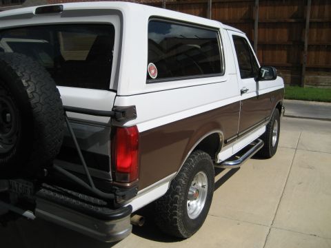White and brown Ford Bronco parked on a driveway, spare tire mounted on the back